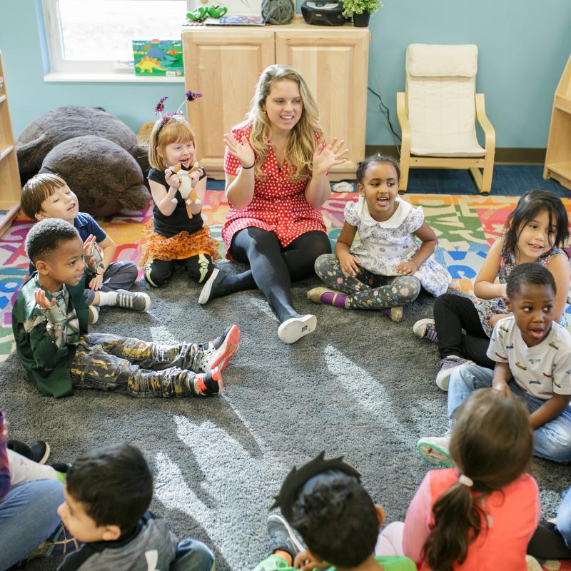 preschool children and teachers seated in a circle and smiling