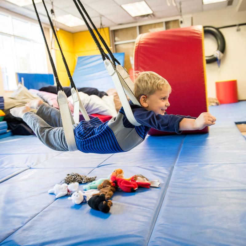 child swinging in a colorful occupational therapy gym